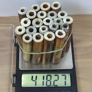 Könnte beinhalten: Ein Bündel aus einundzwanzig zylindrischen, bambusartigen Röhren mit hohlen Zentren und marmorierten weiß-grauen Enden, zusammengehalten von einem grünen Gummiband auf einer Digitalwaage mit einem Gewicht von 418,27 Gramm.