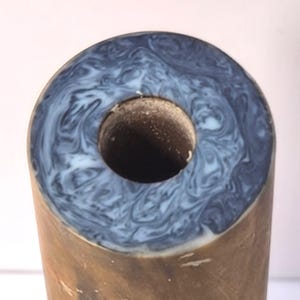 May include: A cylindrical object with a brown exterior and a circular top surface featuring a marbled pattern of dark blue and white swirls. The centre of the top surface has a hollow, circular opening with a textured, light brown interior.