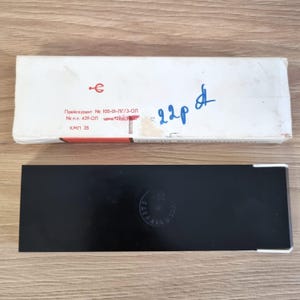 Może przedstawiać: Białe prostokątne pudełko z czerwonymi akcentami i tekstem w obcym języku znajduje się nad czarnym prostokątnym pudełkiem. Białe pudełko ma niebieski odręczny tekst i czerwony symbol. Czarne pudełko ma okrągły emblemat.