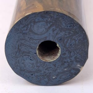 May include: A cylindrical object with a dark blue and black marbled pattern on its circular face. The surface features swirling, organic textures throughout the dark blue and black colours. A circular hole is centred in the middle of the face.