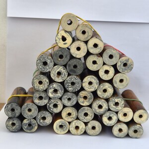 May include: A collection of cylindrical pen blanks stacked in a pyramid shape. Each blank features a central hole and a marbled pattern in shades of cream, grey, and black, or a solid brown wood grain finish, secured together by thin rubber bands.