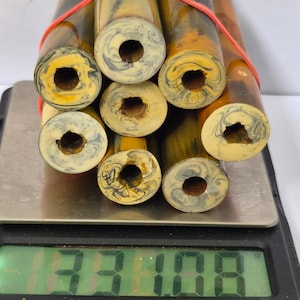 May include: A bundle of seven cylindrical bamboo-like rods with marbled cream and grey ends, secured by a red rubber band and resting on a digital scale displaying a weight of 1331.08 grams. The rods feature a smooth, polished brown finish.