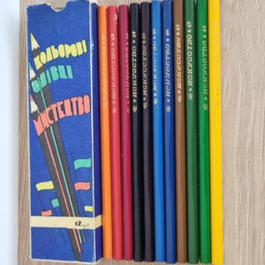 Op de afbeelding: Een set van 12 kleurpotloden in een blauwe doos. De potloden zijn in verschillende kleuren, waaronder oranje, rood, blauw en groen. De doos heeft tekst in een vreemde taal en de woorden "12 шт".