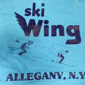 May include: A blue t-shirt with a black graphic of a winged ski logo and the text "ski Wing ALLEGANY, N.Y."