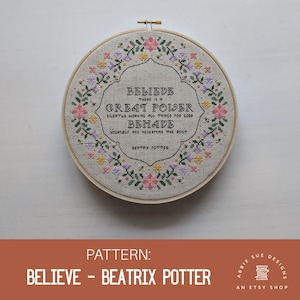 Könnte beinhalten: Stickmuster mit einem Blumenkranz und einem Zitat von Beatrix Potter, das lautet: "Glaube, dass es eine große Kraft gibt, die still und heimlich alles zum Guten lenkt. Benehme dich und kümmere dich nicht um den Rest."