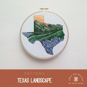 May include: Cross-stitch pattern of the state of Texas with a landscape scene featuring mountains, a river, and bluebonnets. The pattern is in a round embroidery hoop.