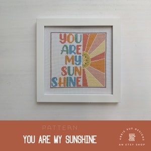 Puede incluir: Patrón de punto de cruz con un diseño de sol radiante de colores y el texto "You Are My Sunshine".