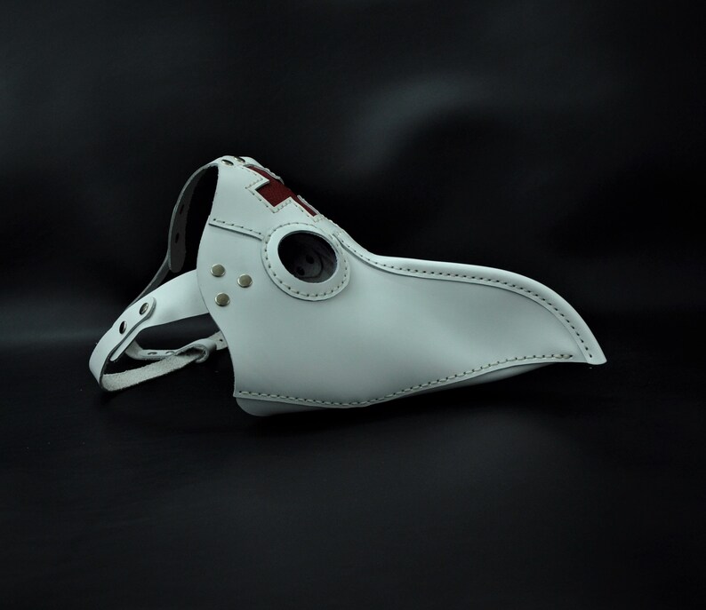 May include: White leather plague doctor mask with a red cross on the beak and a round eye hole.