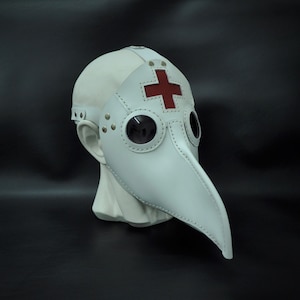 May include: White leather plague doctor mask with a red cross on the forehead and two round eye pieces.