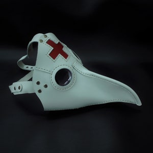 May include: White leather plague doctor mask with a red cross on the front and a round eye piece.