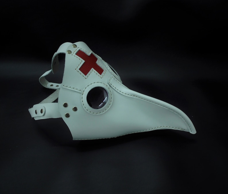 May include: White leather plague doctor mask with a red cross on the front and a round eye piece.