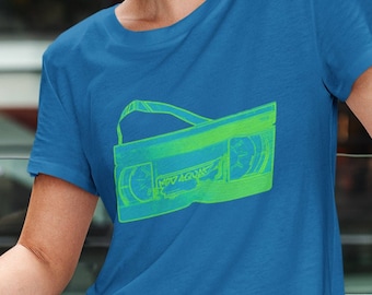 May include: A woman wearing a blue t-shirt with a green and white graphic of a VHS cassette tape. The graphic is a vintage style illustration of a VHS tape.