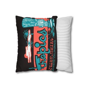 Peut inclure: Un coussin noir avec un design r&eacute;tro avec le mot "Tropics" en turquoise et rouge, ainsi qu'une figure de style tiki. Le coussin porte &eacute;galement le texte "Motor Hotel & Restaurant Modesto, California". Un coussin &agrave; rayures grises et blanches est &agrave; c&ocirc;t&eacute;.