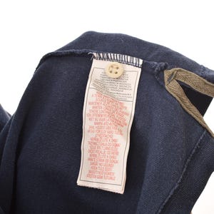 May include: Navy blue polo shirt with a red stripe detail. The shirt features a button-down collar and a tag with text. The collar has a brown trim.