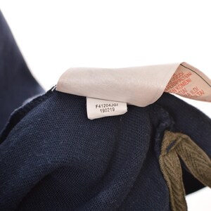 May include: Close-up of a navy blue garment with a tag attached. The tag has the text "F41204JGI 190219" printed on it. The garment has a textured appearance and a contrasting olive green trim.