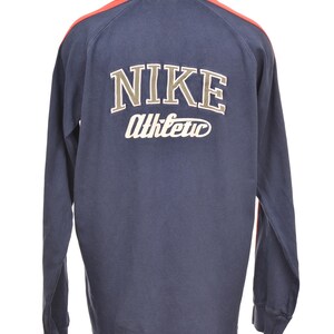May include: Navy blue long-sleeve shirt with the Nike logo and "Athletic" in white lettering on the back. The shirt has a beige collar and red accents on the shoulders. A vintage athletic top.