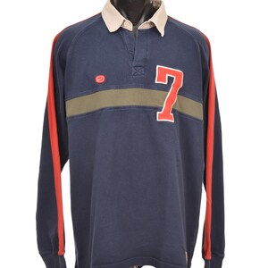 May include: Navy blue long-sleeve rugby shirt with a beige collar and red stripes down the sleeves. Features a green horizontal stripe across the chest and a large white outlined red number 7. The shirt has a button-up collar.