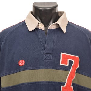 May include: Navy blue long-sleeve shirt with a beige collar and red sleeves. Features a red "7" on the front and a small red Nike logo. The shirt has a green stripe across the chest.