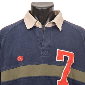 May include: Navy blue long-sleeve shirt with a beige collar and red sleeves. Features a red "7" on the front and a small red Nike logo. The shirt has a green stripe across the chest.
