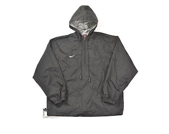 Puede incluir: Una chaqueta negra con capucha, cierre de cremallera y un logotipo Nike swoosh blanco en el pecho izquierdo. La chaqueta tiene una capucha con cordón y un ajuste holgado.