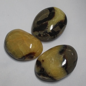 May include: Three smooth, polished stones with a yellow and brown marbled pattern. The stones are oval shaped and have a glossy finish.