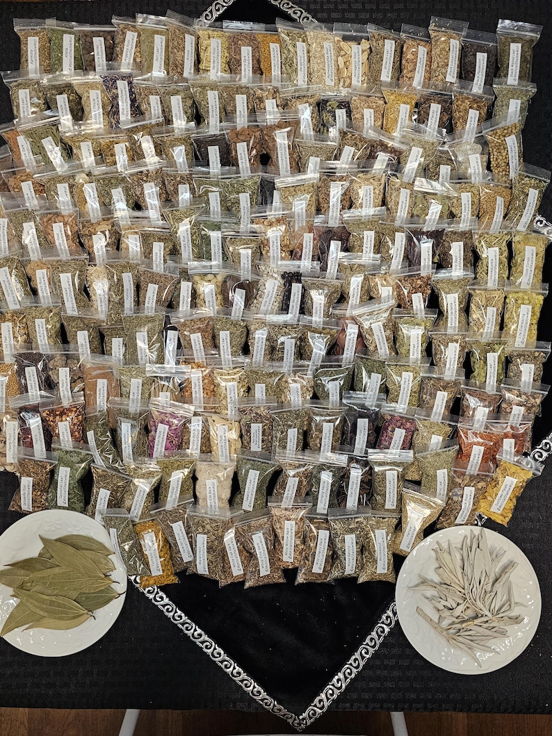 May include: A large collection of small, clear plastic bags filled with various dried herbs and spices. The bags are arranged in a dense pattern, with two white plates holding bay leaves and sage at the bottom. The background is a black surface.