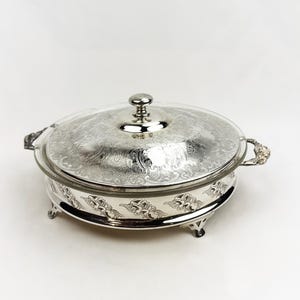 Peut inclure: Plat de service argenté avec un couvercle en verre transparent. Le plat est de forme ovale, avec des motifs floraux ornés et de petits pieds. Le couvercle est orné d'une poignée décorative. Les poignées latérales sont également ornées.