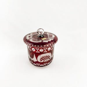 May include: A white ceramic mug with a black handle and the text "But First, Coffee" in a bold, black font. The mug is filled with a dark liquid, likely coffee, and sits on a light-colored surface.