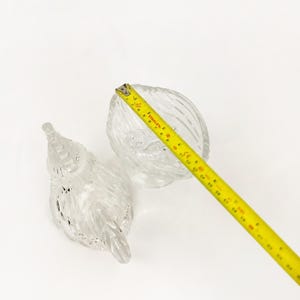 May include: Two clear glass decorative pieces. One is a small bowl with a textured, ridged design. The other is a bird-shaped piece with a textured surface. A yellow tape measure is in the frame, showing measurements in inches.