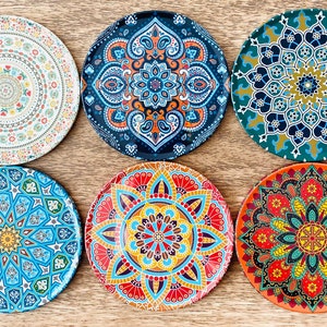 May include: Six round decorative plates with intricate mandala designs in various colors, including blue, green, red, yellow, and white. The plates are arranged in a circle on a wooden surface.
