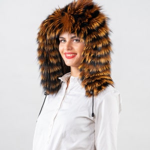 May include: A woman wearing a brown and black fur hood with a white button-down shirt.