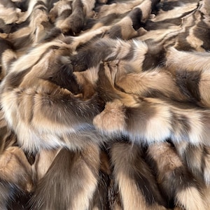 May include: A close-up of a luxurious fur throw blanket made from a variety of furs in shades of brown and beige. The fur is soft and fluffy, and the blanket is perfect for adding a touch of elegance to any room.