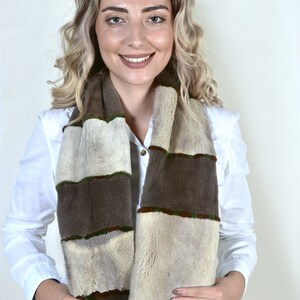 May include: A brown and beige fur scarf with green accents and fringe. The scarf is worn by a person with blonde hair.