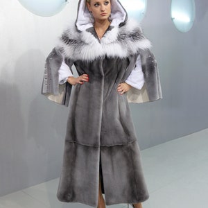 Peut inclure: Un long manteau en fourrure gris avec un col et une capuche en fourrure blanche. Le manteau a une silhouette longue et fluide et est fait d'une fourrure douce et luxueuse.