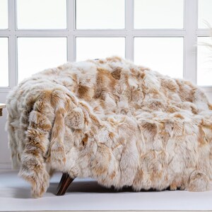 Op de afbeelding: Een luxe nep bont deken in beige en bruine tinten, gedrapeerd over een stoel in een moderne woonkamer.