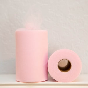 May include: Two rolls of pink tulle fabric. One roll is standing upright and the other is lying down.