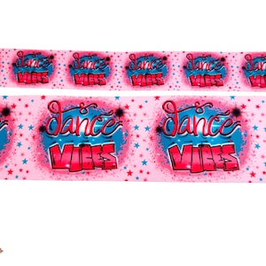 May include: Pink ribbon with a repeating pattern of blue and pink "Dance Vibes" text with white stars.
