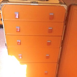 May include: An orange vintage luggage trunk with five drawers and a hinged lid. The drawers have metal handles and the trunk has a leather handle on the top.