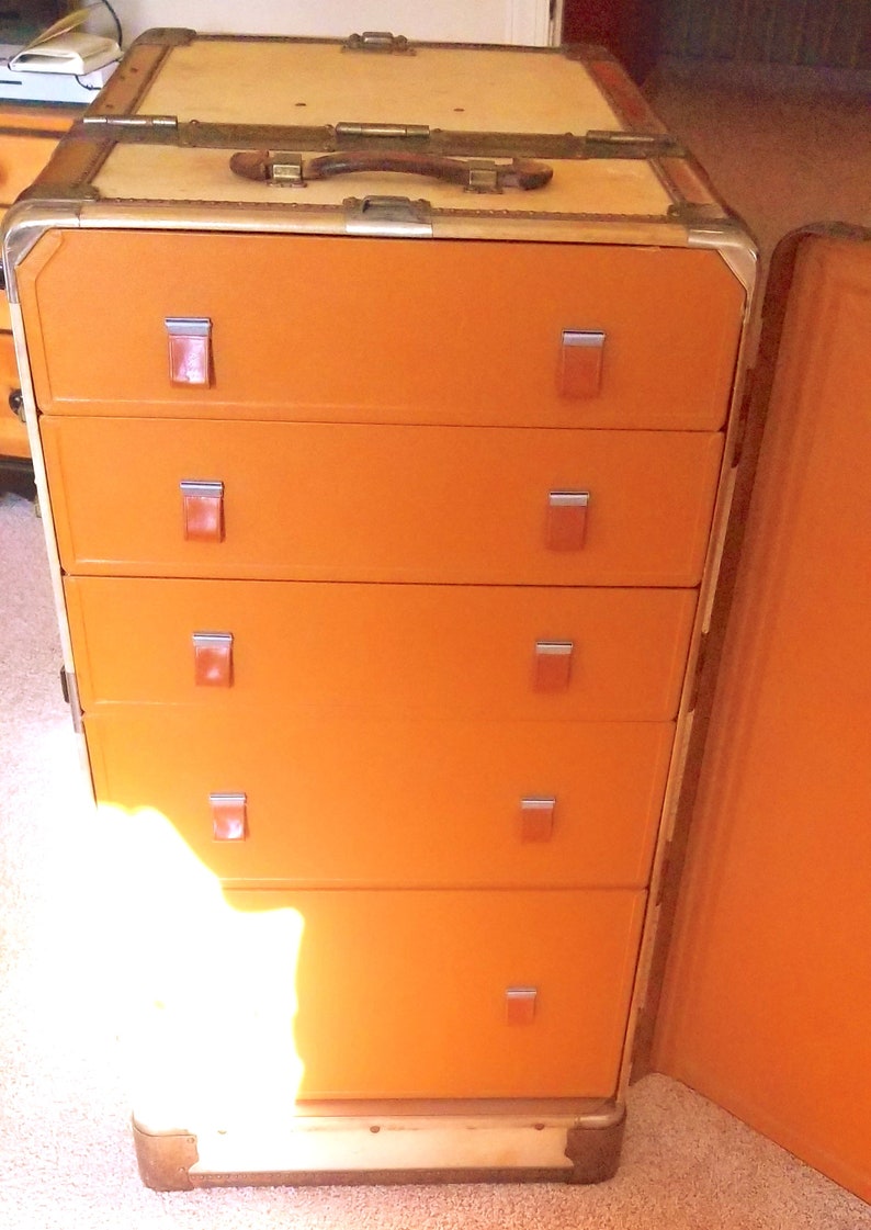 May include: An orange vintage luggage trunk with five drawers and a hinged lid. The drawers have metal handles and the trunk has a leather handle on the top.