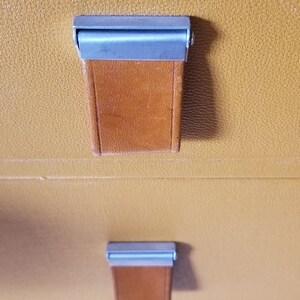May include: Close-up of a set of drawers with brown leather pulls and silver metal accents. The drawers are made of a light brown material.
