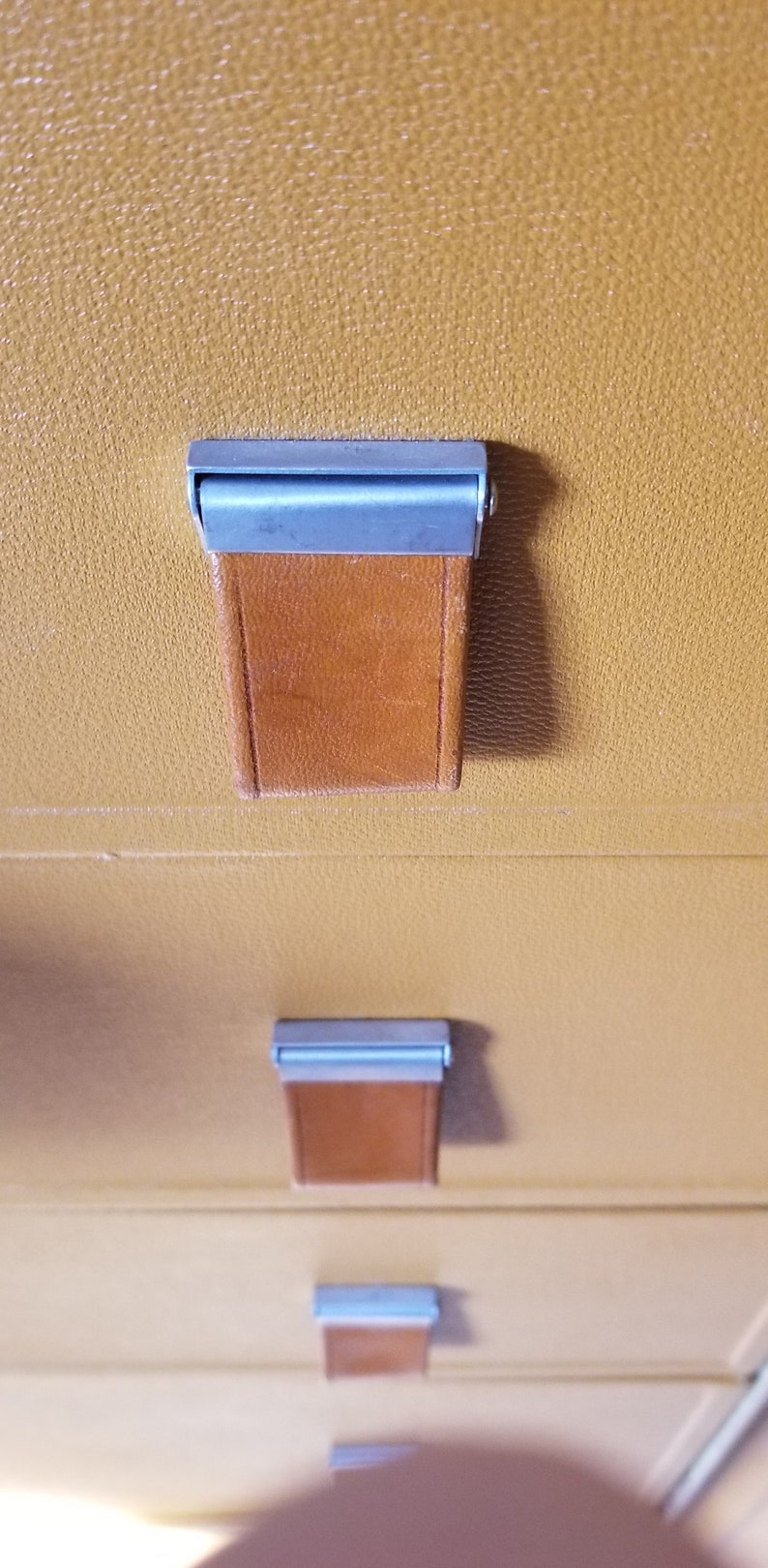 May include: Close-up of a set of drawers with brown leather pulls and silver metal accents. The drawers are made of a light brown material.