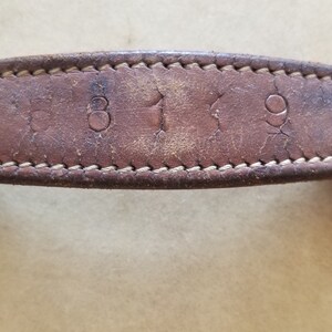 May include: Close-up of a brown leather handle with the numbers "319" embossed on it. The handle is attached to a vintage suitcase.