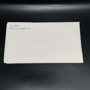 May include: A white envelope with the text "U.S. MINT 1976 Uncirculated Coin" printed in blue. The envelope is rectangular and appears to be made of paper. The background is black.