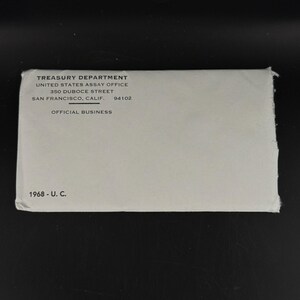 May include: A light gray envelope with the text "TREASURY DEPARTMENT" and "UNITED STATES ASSAY OFFICE" printed in black. The envelope also includes the address "350 DUBOCE STREET, SAN FRANCISCO, CALIF. 94102" and the text "OFFICIAL BUSINESS" and "1968 - U. C."