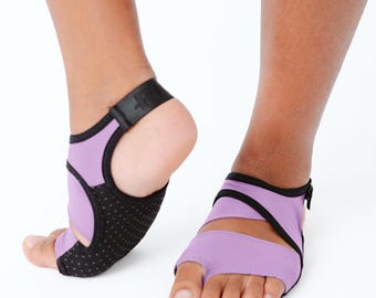 May include: A pair of lavender and black open-toe foot covers featuring a split-toe design, a secure heel strap, and a textured black grip sole. These athletic foot accessories provide coverage across the midfoot and toes with a flexible fabric.