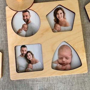May include: Wooden photo puzzle with five cutout shapes: a circle, a pentagon, a square, a triangle, and a knob. Each shape has a photo of a family with a baby.