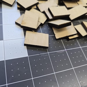 May include: A pile of unfinished wood squares with black edges. The squares are arranged in a random pattern on a black and white grid surface.