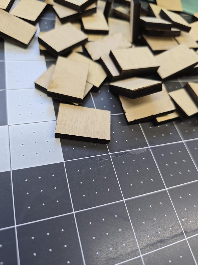 May include: A pile of unfinished wood squares with black edges. The squares are arranged in a random pattern on a black and white grid surface.