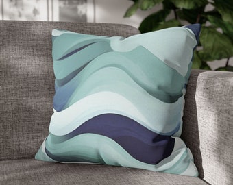 May include: A teal and navy blue cushion with a wavy abstract pattern. The cushion is sitting on a grey sofa.