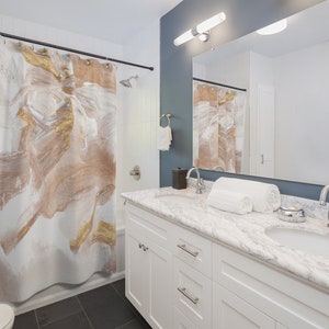 Puede incluir: Un tocador de ba&ntilde;o blanco con una encimera de m&aacute;rmol y dos lavabos. El tocador tiene dos cajones y dos puertas. Una toalla blanca est&aacute; sobre la encimera. El ba&ntilde;o tiene una cortina de ducha con un dise&ntilde;o abstracto dorado y marr&oacute;n.